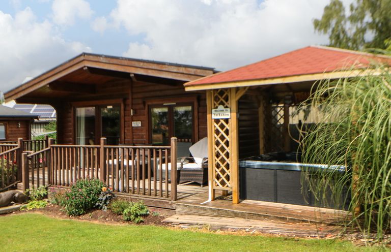 A wooden cabin with railing and outdoor seating next to a covered hot tub on a lawn at Cornfield in Northallerton