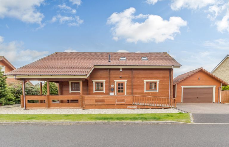 A wooden house with a sloped roof driveway and a garage at Jamaal Lodge in South Broomhill near Amble