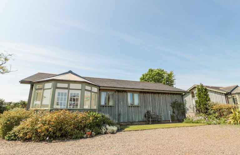 A single-story wooden house with large windows and a garden with shrubs in front at Orchard Lodge in Warkworth