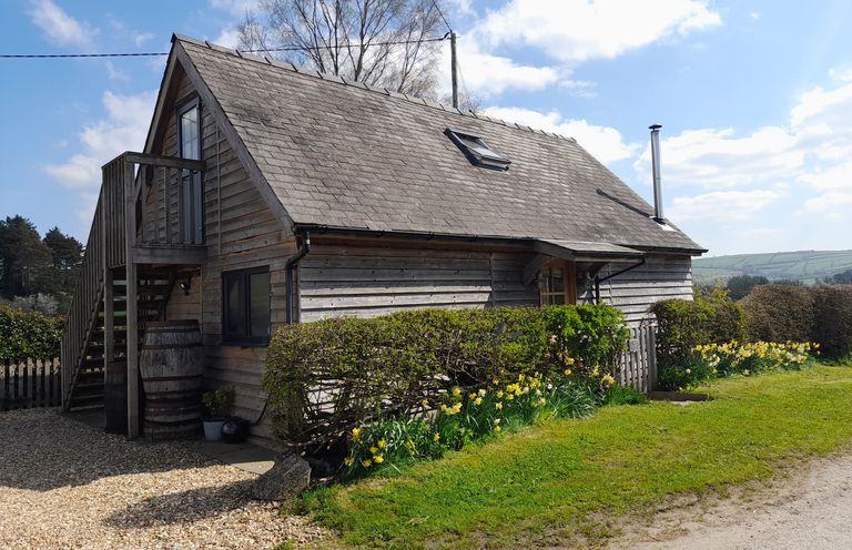A wooden cottage with stairs and a small balcony surrounded by bushes and flowers at Bicton Lodge in Clun
