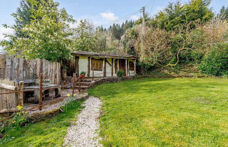 A garden with a grassy lawn a gravel path wooden bench and a small building with timber framing at Brookbank Folly in Mitcheldean