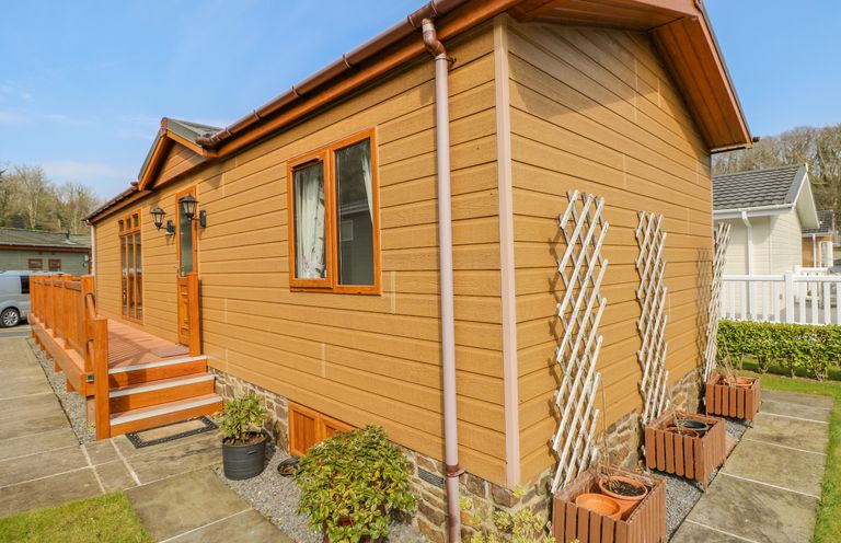 Exterior of a wooden cabin with a small porch steps and potted plants at Cladebrine Wisemans Bridge near Saundersfoot