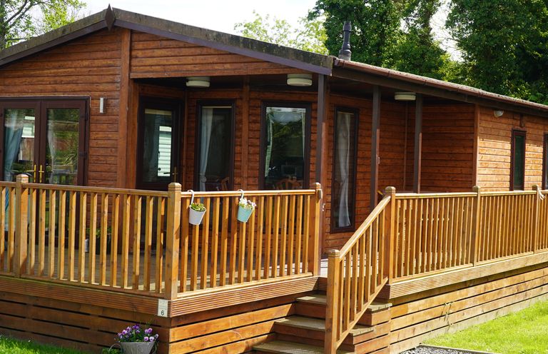 A wooden cabin with a railing and steps leading to a porch with potted plants at Roe Deer Lodge in Castlewigg near Whithorn