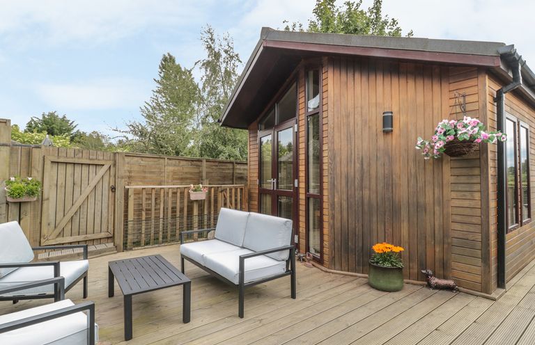 An outdoor seating area with chairs a table and a wooden building at Little Gem Lodge Charlesfield near St Boswells