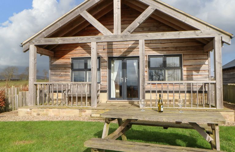 A wooden cabin with a porch and a picnic table on a lawn at Coquet in Longframlington near Alnwick