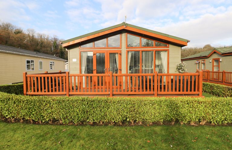A single story cabin with a wooden deck and hedges in front at The Retreat in Wisemans Bridge near Saundersfoot