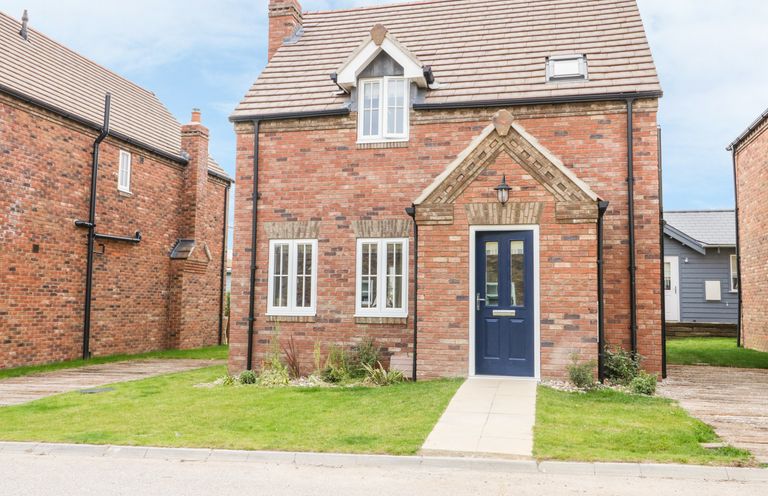 A brick house with a blue door and three windows and a small lawn at Flip Flops The Bay near Filey
