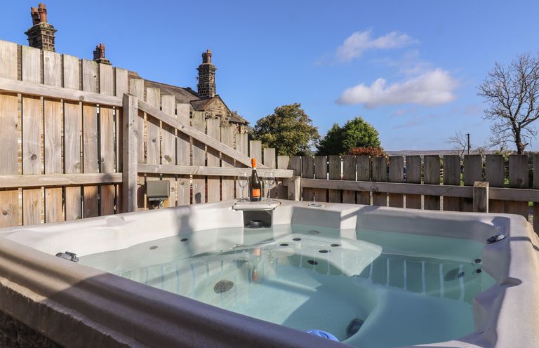 An outdoor hot tub with a bottle of wine and two glasses on a wooden tray by a wooden fence at The Old Hen Shed in Hainworth near Haworth