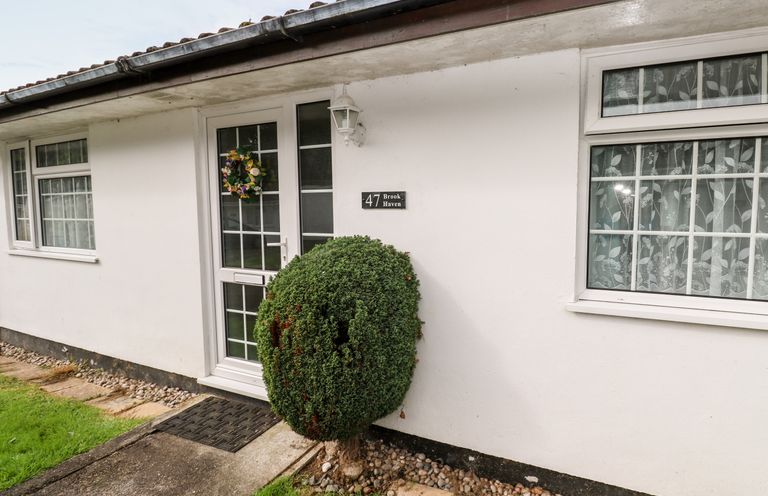 Front entrance of a white house with a trimmed round bush near the door and windows at Brook Haven Rosecraddoc Lodge near Liskeard Cornwall