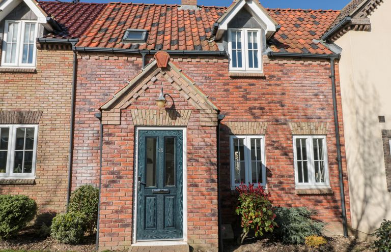 Front view of a brick house with a blue door and windows with white frames at Dotty's Sunshine Cottage in The Bay near Filey
