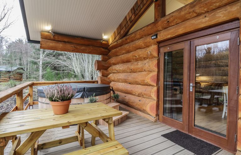 An outdoor wooden deck with a picnic table, a potted plant, a hot tub, and glass double doors at Moorhen Lodge in North Kessock