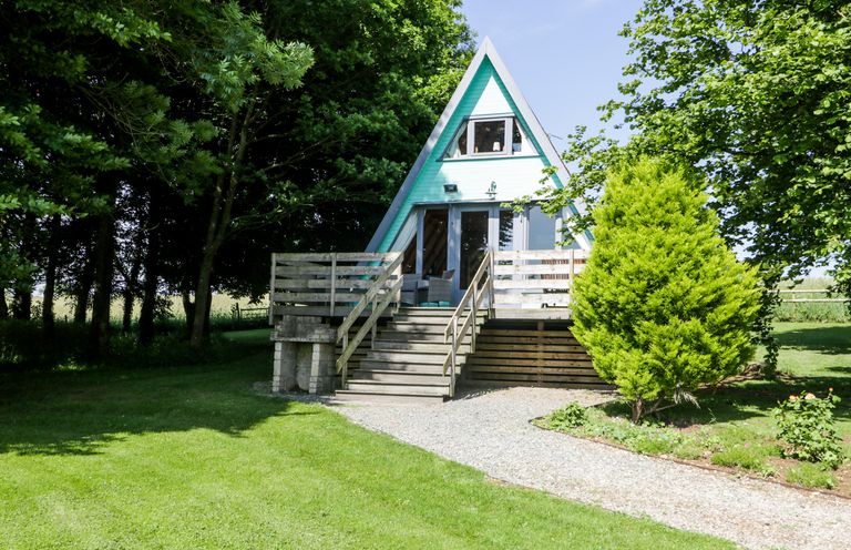 A small A-frame house with a wooden deck and stairs surrounded by trees and grass at Apple Tree Lodge in Gillingham