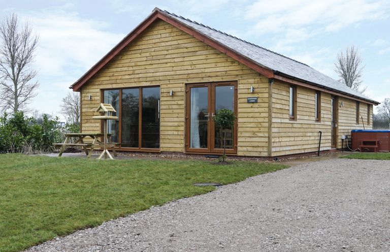 A wooden lodge with patio doors and picnic table on grass next to a gravel path at Gardeners Lodge in Nantwich