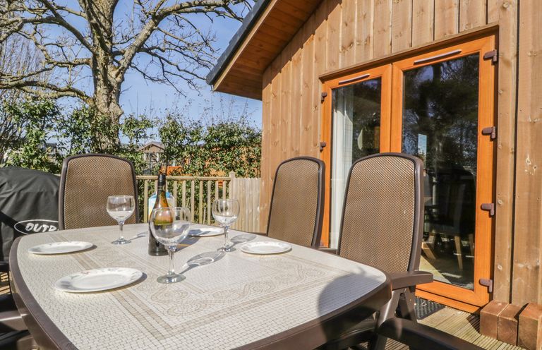 An outdoor table with plates and wine glasses set on a wooden deck outside a wooden building at Holmedell in Greystoke