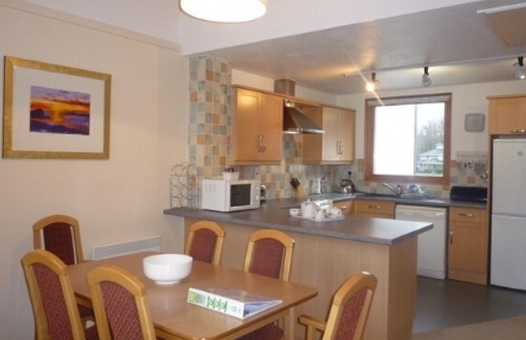 A kitchen and dining area with a wooden table and chairs a microwave countertop appliances and a window at 17 Keswick Bridge in Keswick