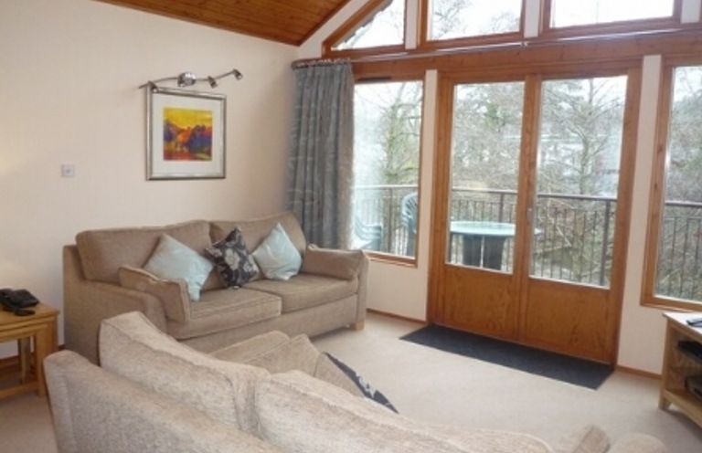 A living room with two beige sofas cushions a framed picture on the wall and glass doors leading to a balcony at 13 Keswick Bridge in Keswick