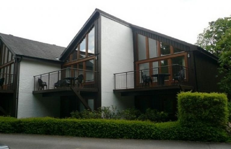 A modern multi-unit building with balconies and glass windows surrounded by greenery at 10 Keswick Bridge in Keswick