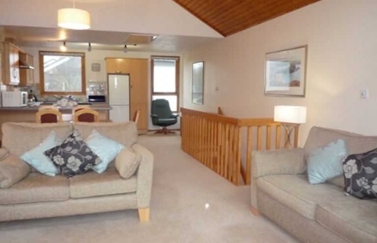 A living room with sofas and cushions and a kitchen area with a refrigerator and dining chairs at 16 Keswick Bridge in Keswick