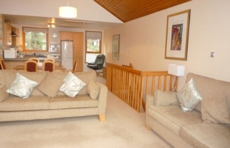A living room with two beige sofas and a wooden railing with an open kitchen and dining area in the background at 20 Keswick Bridge in Keswick