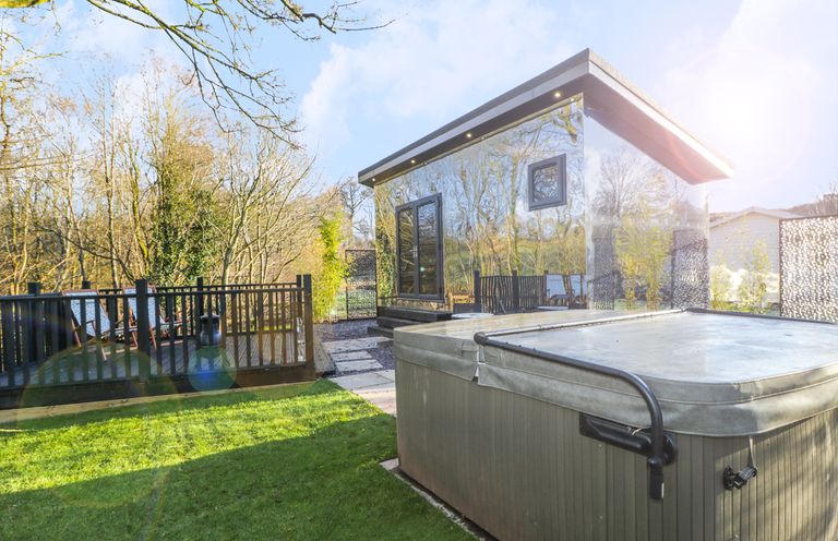 A garden with a hot tub and a mirrored cabin near a deck with chairs at Reflection in Longtown