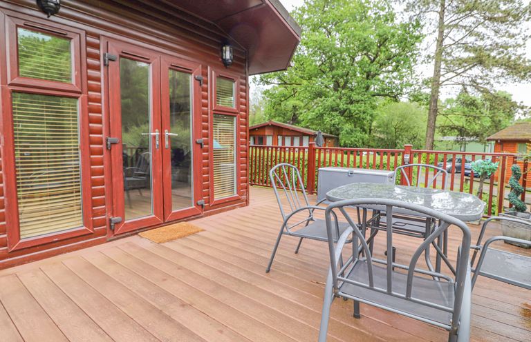 A wooden deck with metal chairs and a table outside a cabin at 10 Thirlmere White Cross Bay near Troutbeck Bridge