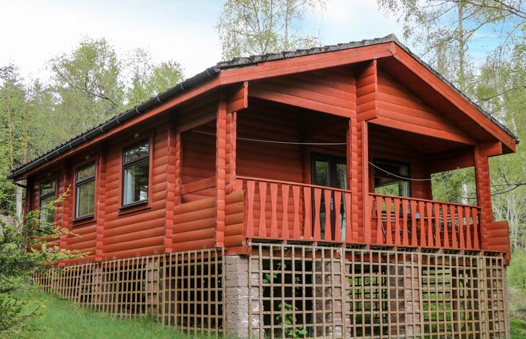 A wooden cabin on a raised platform surrounded by trees and grass at Eagle Lodge in Strathpeffer