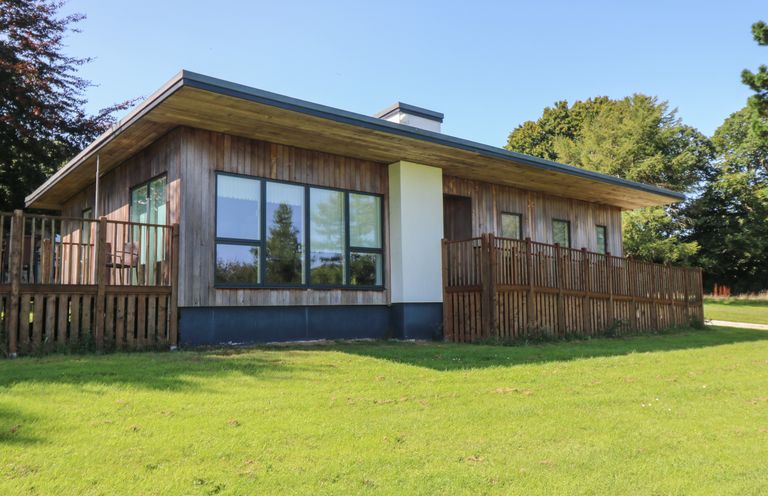 A wooden cabin with large windows and a fenced patio on a grassy lawn at Hazel in Truro