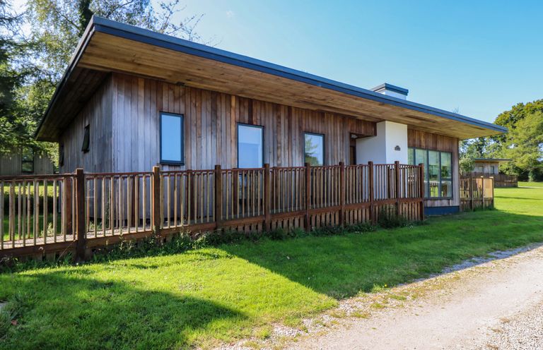 A wooden house with a fenced porch on a grassy area at Juniper in Truro
