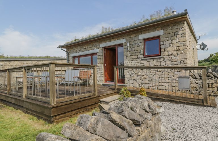 A stone house with a wooden deck and outdoor furniture surrounded by a stone wall at Boavista in Carnforth
