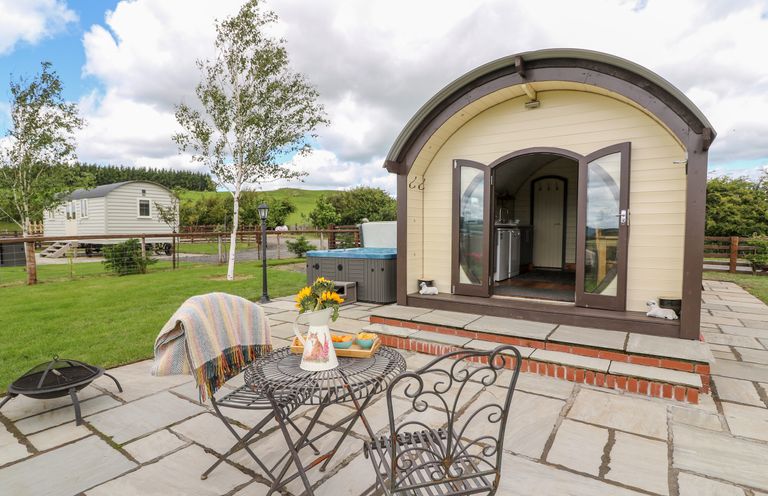 An outdoor patio with a metal table and chairs a small building with open doors and green grass at Mountain View in Rhayader