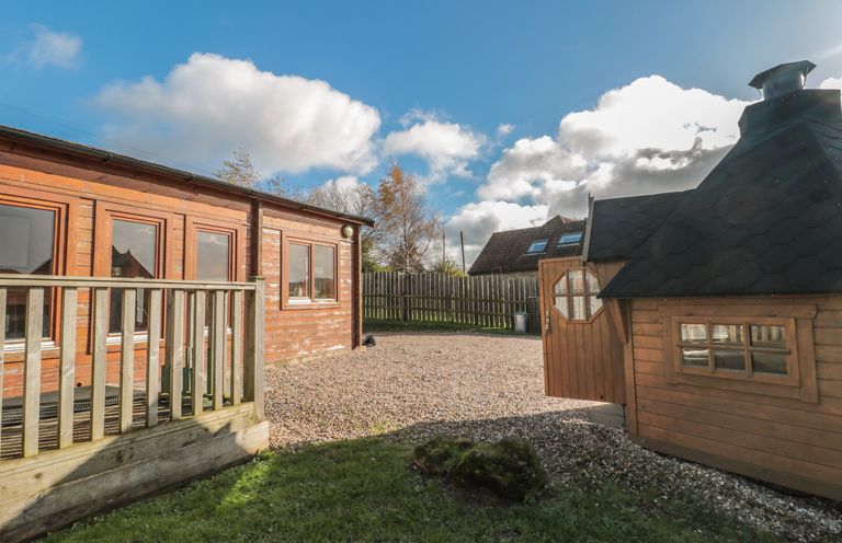 An outdoor area with a wooden building and a small wooden cabin with a gravel ground and a wooden fence at Sunnyside Lodge in Crewkerne