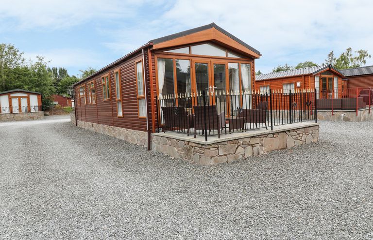 A gravel driveway with multiple wooden lodges and an outdoor seating area at 32 Cruachan Lodge in Auchterarder