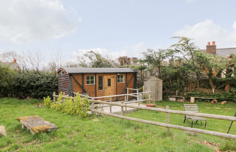 A wooden cabin with a fenced garden bench and trees at Railway Carriage in Govilon