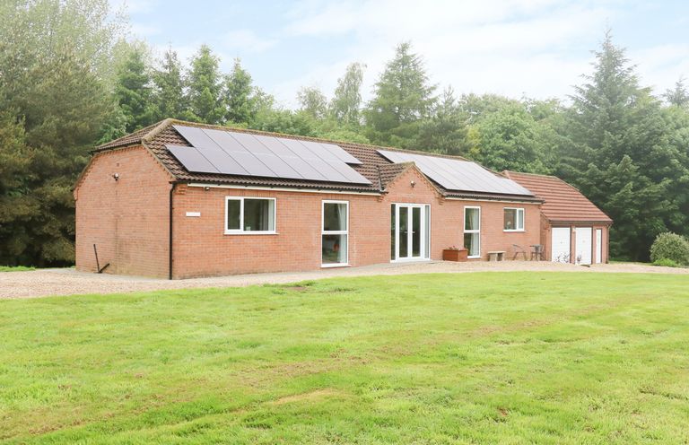 A single story brick house with solar panels on the roof and a garage surrounded by grass and trees at Heron Lodge in Mavis Enderby near Spilsby