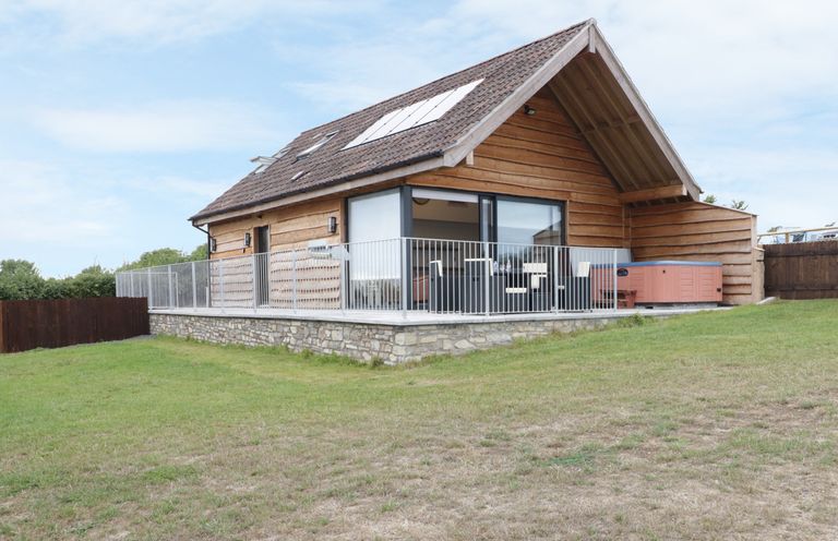 A wooden cabin with a balcony, outdoor seating, and a hot tub on a grassy area at Swan Lodge Castle Farm in Wedmore