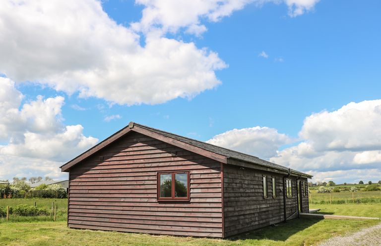 A single wooden cabin with several windows on a grassy field under a blue sky with clouds at Rose Lodge in Sheriff Hutton