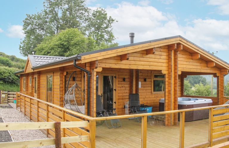 A wooden lodge with a deck and hot tub at Manor Farm Lodges - Red Kite Lodge in Newtown