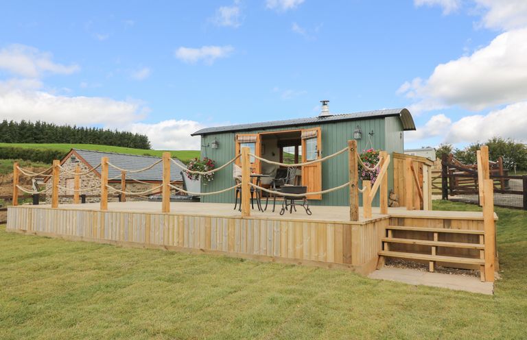 A small green cabin on a raised wooden deck with outdoor furniture and stairs leading to a grassy lawn at Ivy's Way in Rhayader
