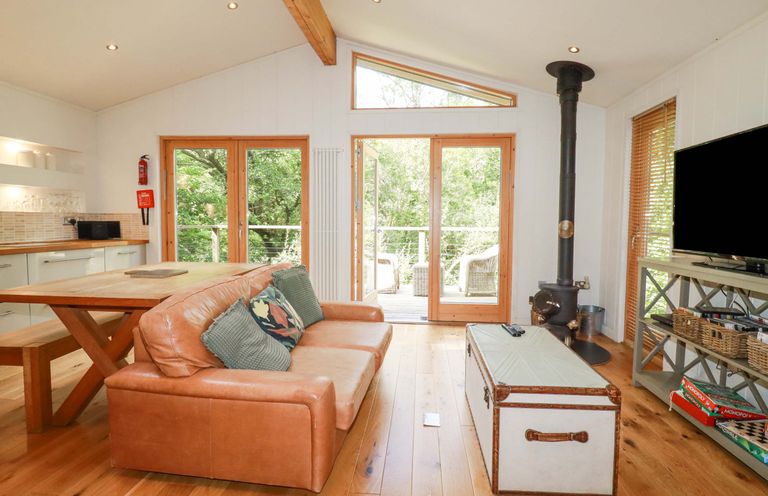 A living room with a leather sofa wooden table glass doors and a wood stove at 4 Stonerush Valley in Lanreath