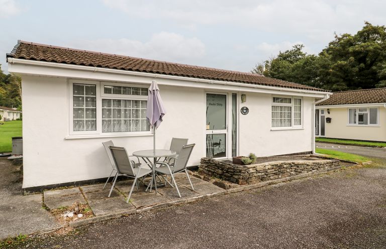 A single story white building with two windows a glass door and an outdoor table with four chairs and an umbrella at Ducks Ditty in Liskeard