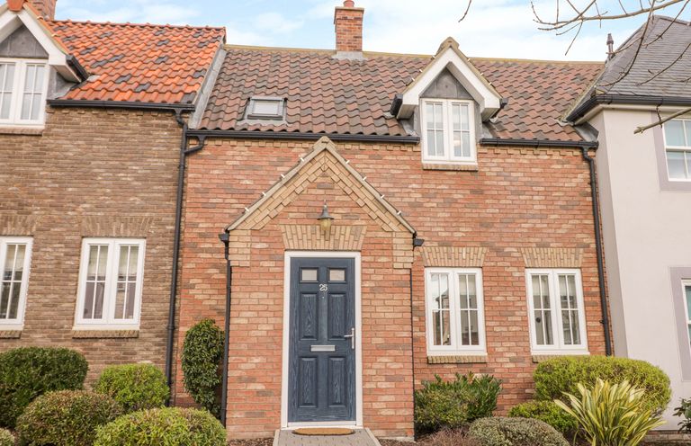 A brick house with a blue door and multiple white framed windows surrounded by shrubs at Bayside Cottage The Bay near Filey