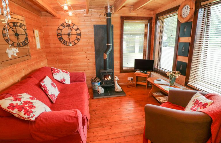 A wooden living room with a red sofa and armchair a wood stove and a small TV at The Lodge in Rosemarket