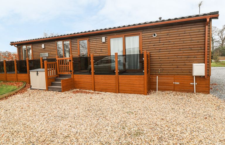 A wooden lodge with glass doors and windows surrounded by a gravel driveway at Avonal Lodge (24) in Dunning